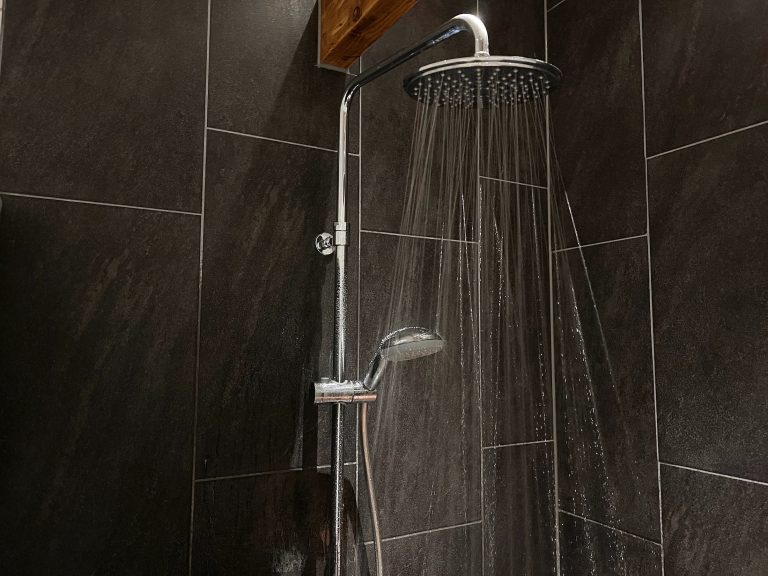 Showerhead releasing water in a modern bathroom with dark tiling-Leak repair Ashfield
