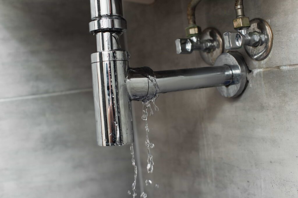 Leaking chrome water pipe near shut-off valves on tiled wall 