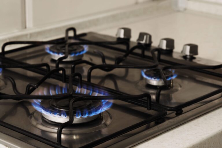 Close-up of a gas cooktop with blue flames lit on the burners, showcasing active cooking-Gas Appliance Installation Floreat