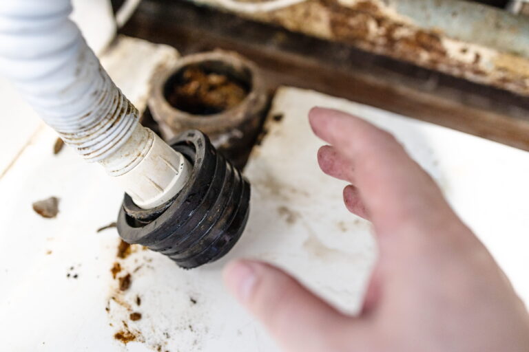 A plumber's hand near a corroded drain hose with dirt buildup-Blocked Drain Cleaning Ashfield