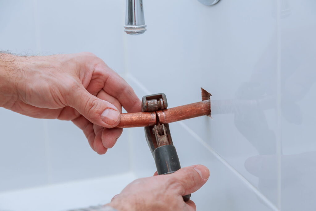 Plumber cutting a copper pipe with a pipe cutter for burst pipe repair  work-Burst pipe repair Beldon