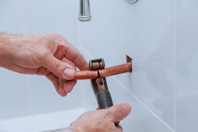 Plumber cutting a copper pipe with a pipe cutter for burst pipe repair  work