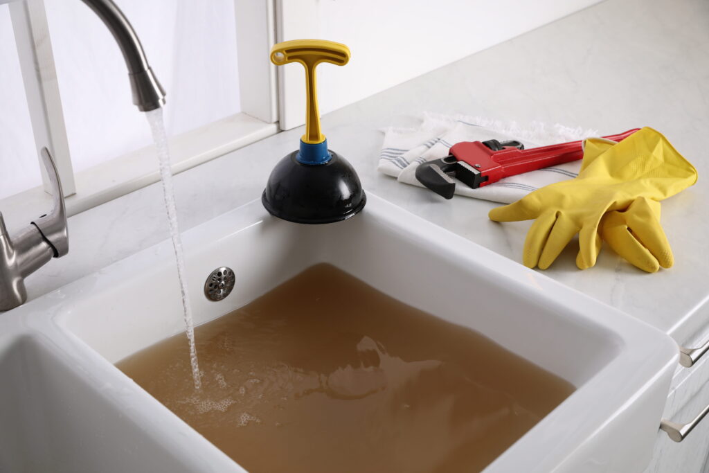 Blocked Drain Emergency Perth: Signs It Can't Wait 3 Blocked kitchen sink with dirty water and plunger, rubber gloves, and wrench on the counter