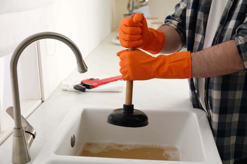 A plumber in orange gloves plunging a blocked kitchen sink with dirty water-Blocked Drain Cleaning Ashfield